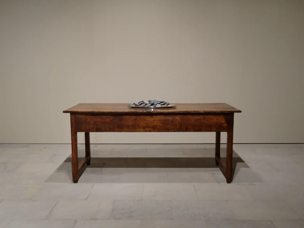 Llengua paterna. "Un cop de fuet fa un blau, però un cop de llengua trenca els ossos", 2022 Plata d'alpaca, talla de còdols, taula 95 x 194 x 78 cm